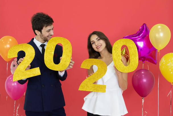 Junges Paar feiert gemeinsam Neujahr und hält glitzernde Buchstaben vor rotem Hintergrund in die Höhe. - Foto, Bild