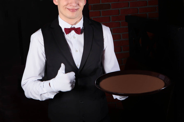 Un camarero con guantes blancos sostiene un puño con el pulgar hacia arriba. Foto irreconocible sin rostro. Copiar espacio
. - Foto, imagen