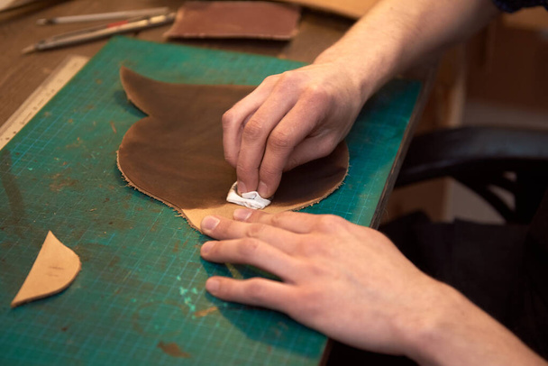 Close up de couro mestre mãos tingimento de couro natural na mesa de trabalho. Mãos masculinas de mestre tingimento de couro genuíno. Fabricação de artigos de couro feitos à mão
. - Foto, Imagem