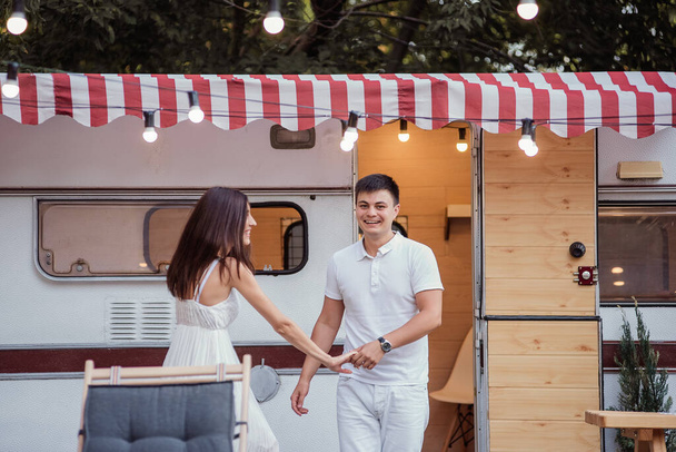 A young beautiful couple travels around the country together on a trailer. A girl in a white long dress, a guy in shorts and a light T-shirt - Foto, immagini