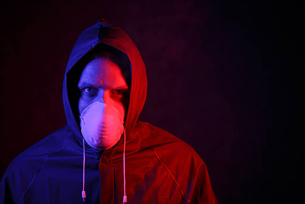 Coronavirus. Een man met een masker en een chemisch beschermingspak in rood en blauw licht. Bestrijding van het virus - Foto, afbeelding