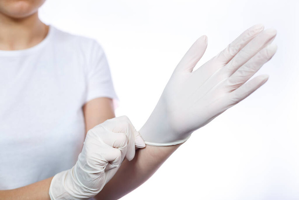 Girl paramedic puts on white medical gloves on hands. Protection against germs and viruses. She is in a white T-shirt on a white background. - Foto, Imagem