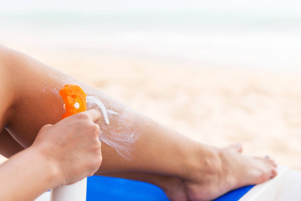 Meisje gebruikt spray om zonnecrème aan te brengen op haar been op het strand. - Foto, afbeelding