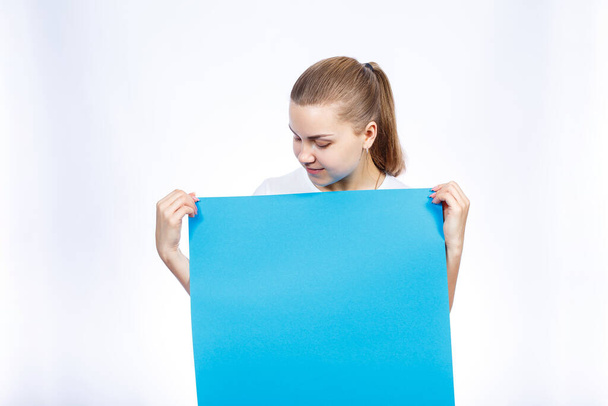 Een meisje in een wit T-shirt houdt in haar handen een blauw blanco groot banner. - Foto, afbeelding