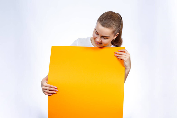Une fille dans un T-shirt blanc tient une bannière orange vierge grande feuille
. - Photo, image