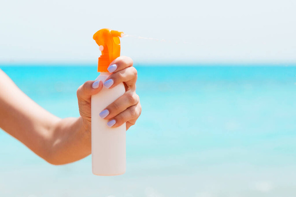Abgeschnittenes Bild der Hand einer Frau mit Sonnenschutzspray am Strand. - Foto, Bild
