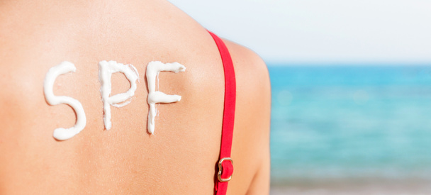 Palabra SPF hecha de protector solar en la espalda de la mujer en la playa. Concepto de factor de protección solar
. - Foto, Imagen