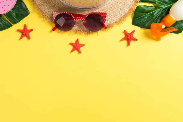 Beach accessories with straw hat, sunscreen bottle and seastar on yellow background top view with copy space. - Foto, Bild