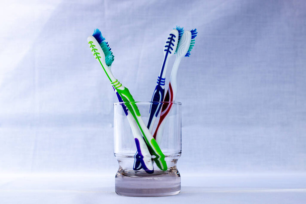 Beyaz arka planı olan şeffaf bir cam bardakta çeşitli renkli diş fırçaları. - Fotoğraf, Görsel