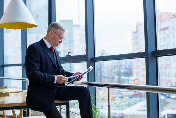 Man managing director leaned on a wooden table in his office near a large window and looks at a successful business development plan. - Photo, Image