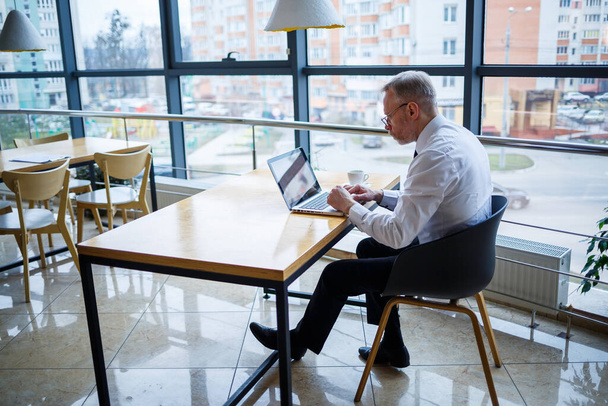 Homme freelance travaille dans un café sur un nouveau projet d'entreprise. Assis à une grande fenêtre à la table. Regarde un écran d'ordinateur portable avec une tasse de café
 - Photo, image