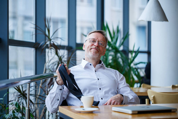 Adult male manager businessman worked successfully and at the end of the day drinks coffee without a jacket - Fotoğraf, Görsel