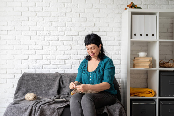Zůstaň doma. Usmívající se žena středního věku se těší doma a pletení sedí na pohovce - Fotografie, Obrázek