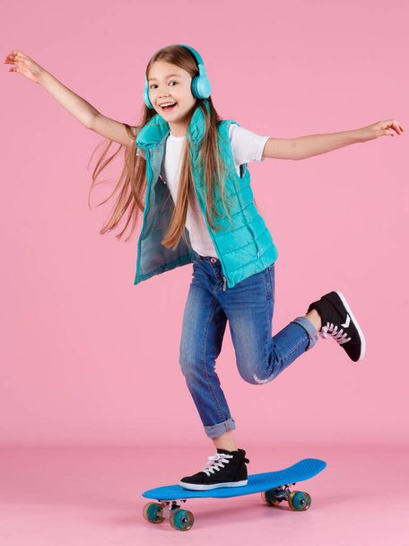 Beautiful little blonde kid girl 7-10 years old in jacket posing isolated on pastel pink background children portrait. Childhood lifestyle concept. Mock up copy space. Hold blue skateboard - Foto, immagini