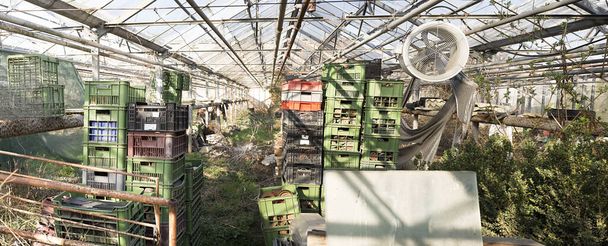 Sérült és elhanyagolt mezőgazdasági üvegház egy hatalmas ventilátor és rengeteg virágcserép, rendetlenség. Hiányzó és törött üveg - Fotó, kép