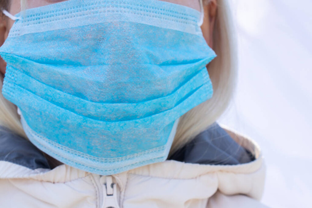closeup of a young Ukrainian woman in a medical mask on her face during the pandemic outdoors - Photo, Image