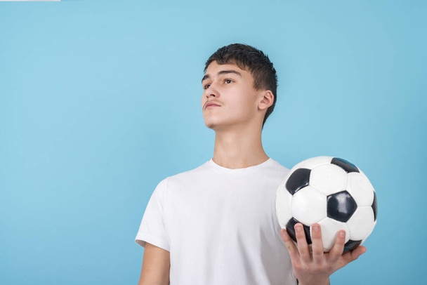 Plan studio d'un adolescent tenant la balle dans ses mains et regardant fièrement loin sur fond bleu. Concept de mode de vie sain
 - Photo, image