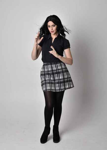 Portrait of a goth girl with dark hair wearing blue and plaid skirt with boots. Full length standing pose on a studio background. - Photo, Image
