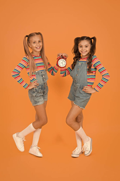 Small children smiling with mechanical clock. School clock. Timing personal plan and schedule. Counting time concept. Dead line. Happy little girls hold vintage alarm clock on orange background - Valokuva, kuva