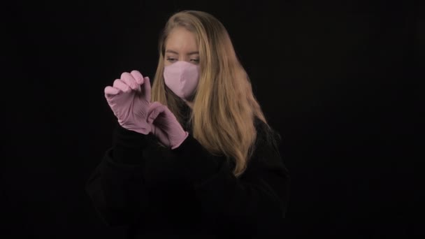 Girl in pink medical mask straightens pink gloves on hand. Isolated on black background. Health care and medical concept. Close up portrait . 4k. Coronavirus Epidemic, illness, pandemic - Metraje, vídeo