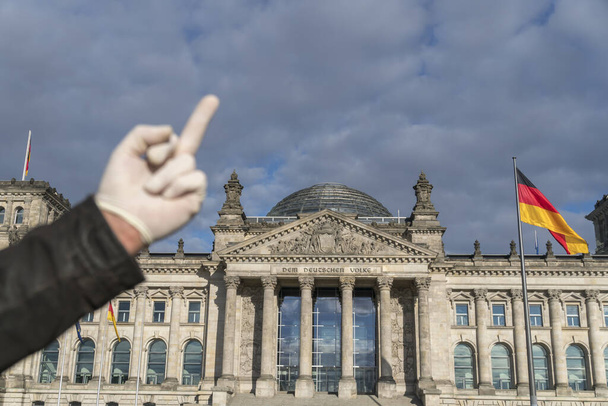 Hand with latex gloves giving German Bundestag in Berlin the middle finger. Selective focus - Фото, изображение