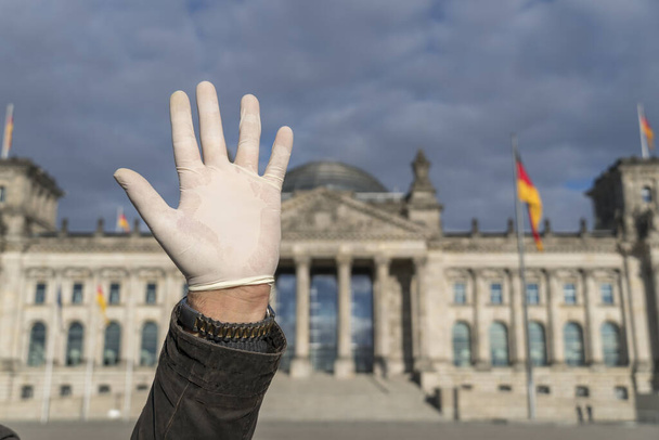 Hand met latex handschoen die afscheid neemt van de Duitse Bondsdag in Berlijn. Selectieve focus - Foto, afbeelding