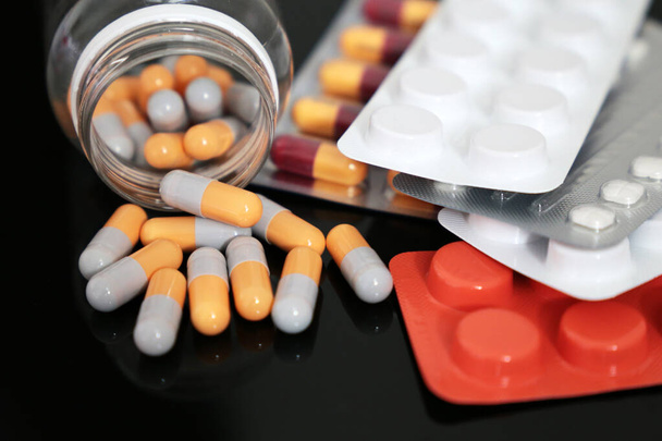 Tabletták egy sötét üvegasztalra, gyógyszerek tablettákban és kapszulákban szétszórva egy üvegből. A koronavírus-védelem, gyógyszertár, antibiotikumok vagy vitaminok fogalma - Fotó, kép
