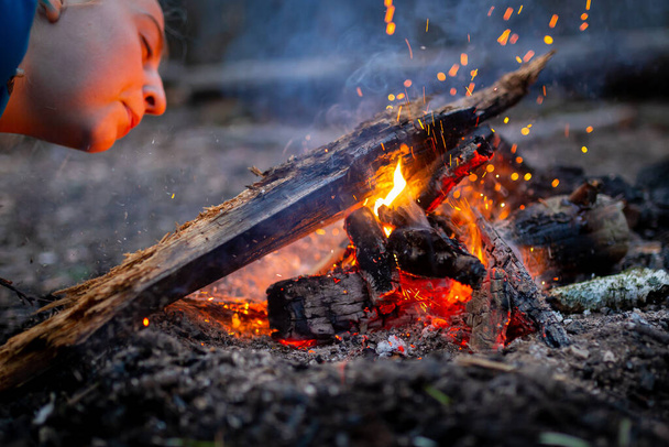 Femme soufflant un feu avec des étincelles dans la forêt de camping de plein air
 - Photo, image