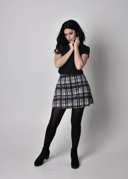 Retrato de uma menina gótica com cabelo escuro vestindo saia azul e xadrez com botas. Posse de pé de comprimento total em um fundo de estúdio
. - Foto, Imagem