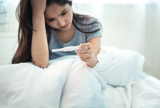 Young depressed and desperate Asian young woman crying and scared testing positive result on pregnancy test alone in bed feeling depressed, remorse and stress in irresponsible mistake concept - Photo, Image