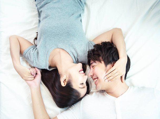 幸せとかなり若いアジアのカップルの肖像画。アジアの男と女は大きな笑顔で向かい合ってベッドに横になって. - 写真・画像