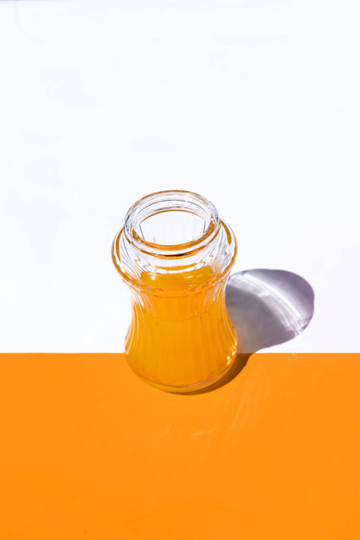 白とオレンジの背景にオレンジジュースが入った垂直方向のビューグラスで二つの半分と容器を中心に - 写真・画像