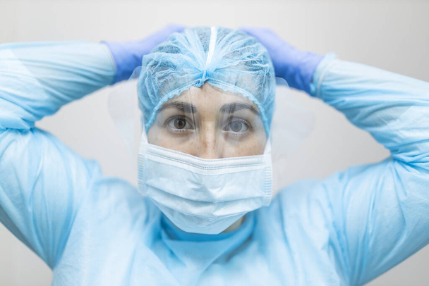 junge Krankenschwester bindet ihre Atemschutzmaske mit Schutzkleidung - Foto, Bild