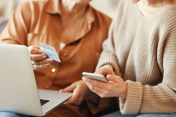 Crop donne in abiti casual utilizzando laptop e smartphone durante lo shopping online con carta di credito in plastica a hom
 - Foto, immagini