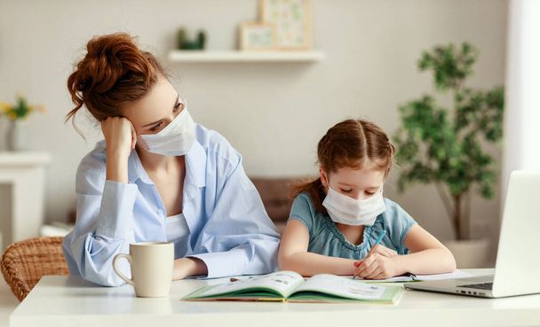 Exhausted woman in medical mask sitting at table and watching diligent girl writing in notebook while doing homework together during pandemi - Photo, Image