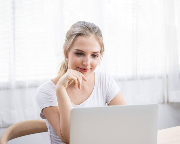 Beautiful happy caucasian woman in casual communicate via computer by video chat in living room.Work at home,stay at home and social distancing concept. - Photo, image