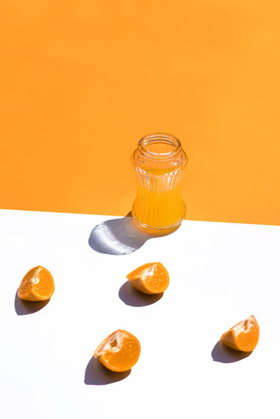 boční pohled skleněný pohár s pomerančovou šťávou na bílém a oranžovém pozadí vytváří dvě poloviny a kontejner na střed, čtyři oranžové segmenty na bílém, vertikální - Fotografie, Obrázek