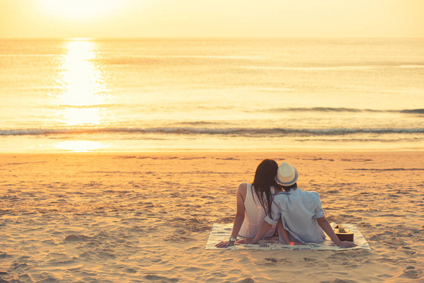 Rakastunut pariskunta katselee auringonlaskua yhdessä rantalomalla. Ihmiset siluetti takaapäin istuu nauttien näkymä auringonlaskun merelle trooppinen kohde loma. Romanttinen pari rannalla. - Valokuva, kuva
