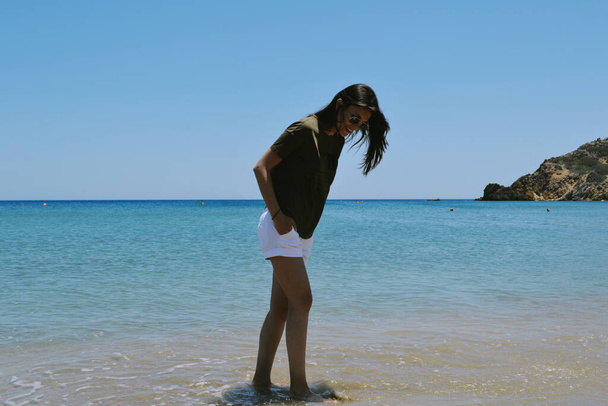 Λευκή γυναίκα με λευκό σορτς και σκούρο t-shirt στέκεται σε μια παραλία σε ένα καλοκαίρι - Φωτογραφία, εικόνα