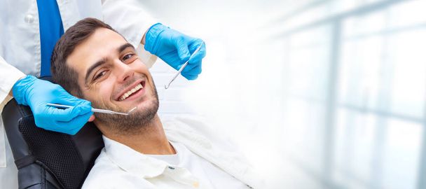 молодой человек в стоматологической клинике с инструментами и руками стоматолога
 - Фото, изображение