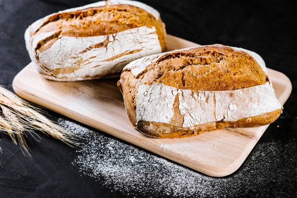 sweet and tasty bread and wheat on black wooden background - Foto, immagini