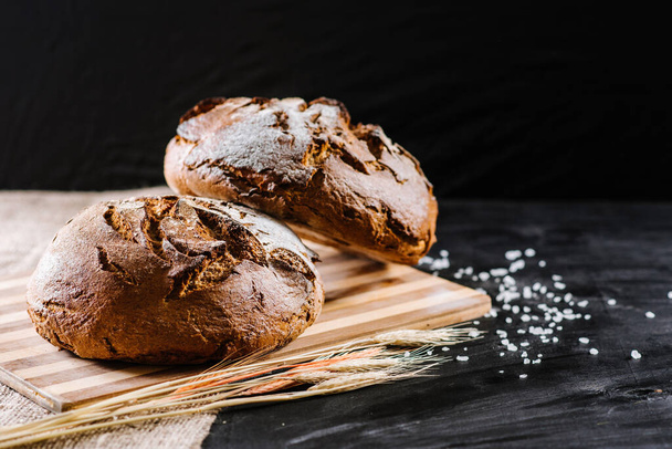 sweet and tasty bread and wheat on black wooden background - Foto, Imagen