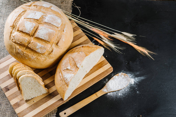 Sweet fresh bread and wheat on black wooden background - Foto, imagen