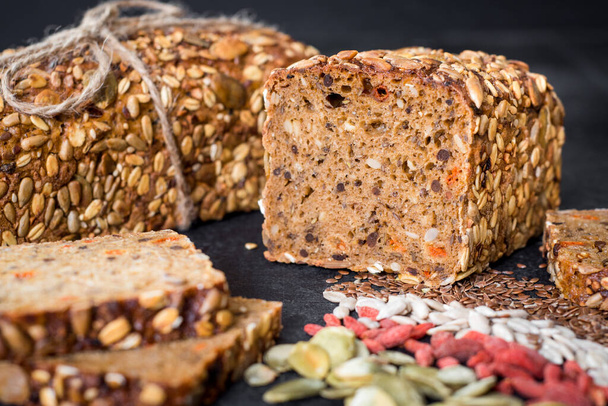 Tasty sweet rye bread with seeds on black wooden background - Foto, afbeelding