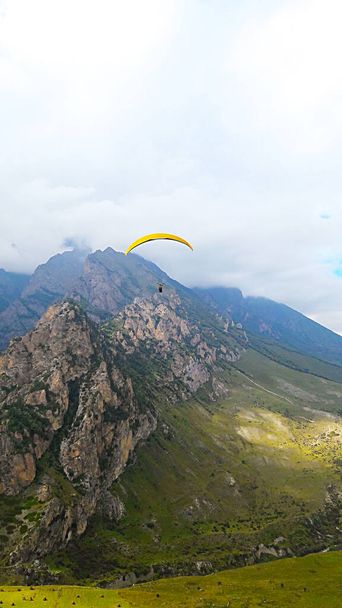 Парагвайдери літають у хмарному небі з жовтим парашутом у горах
 - Фото, зображення