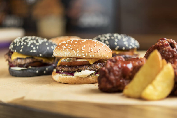 hambúrgueres com rolos amarelos e pretos sobre pergaminho com asas de frango empanadas e batatas fritas
 - Foto, Imagem