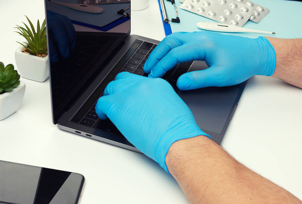 specialist doctor in blue latex medical gloves working on a laptop, concept of remote maintenance, therapist's workplace, top view - Photo, Image