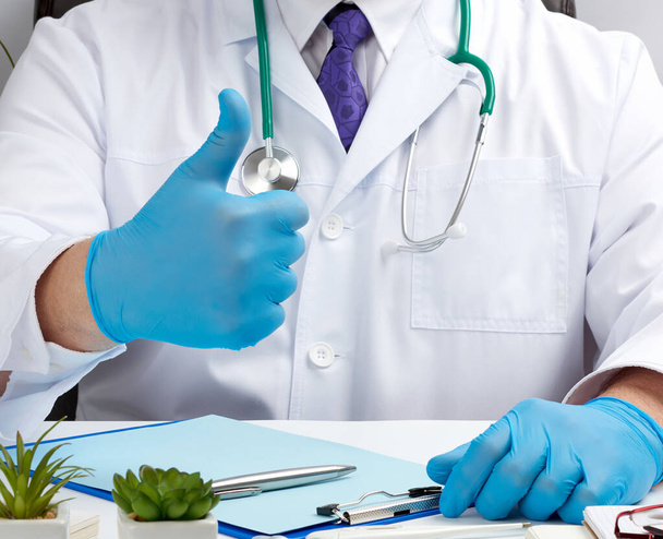 médico de casaco branco e gravata mostra com a mão um gesto como, vestindo luvas médicas de látex azul, close-up
 - Foto, Imagem