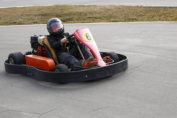 Chłopak prowadzi gokartowy samochód z prędkością na torze wyścigowym na placu zabaw. Go kart jest popularnym sportem motorowym rekreacji. - Zdjęcie, obraz