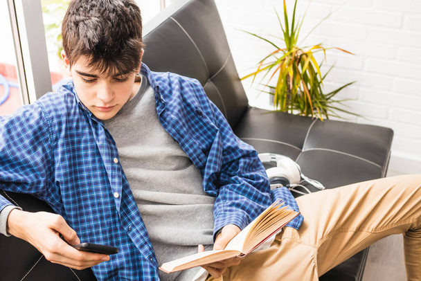молодий хлопчик-підліток з мобільним телефоном і книгами вдома або в квартирі
 - Фото, зображення